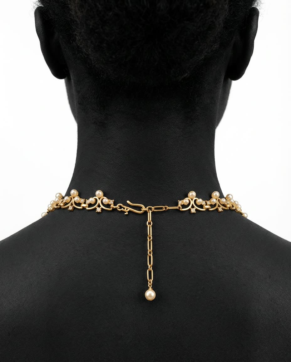 A gold necklace fastened at the nape of a neck, against black